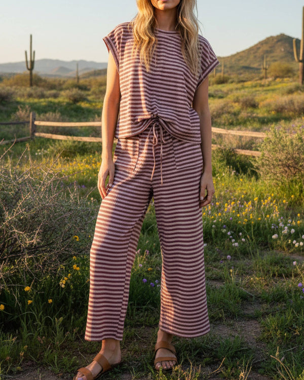 Woman in a striped outfit standing in a desert landscape with mountains in the background.