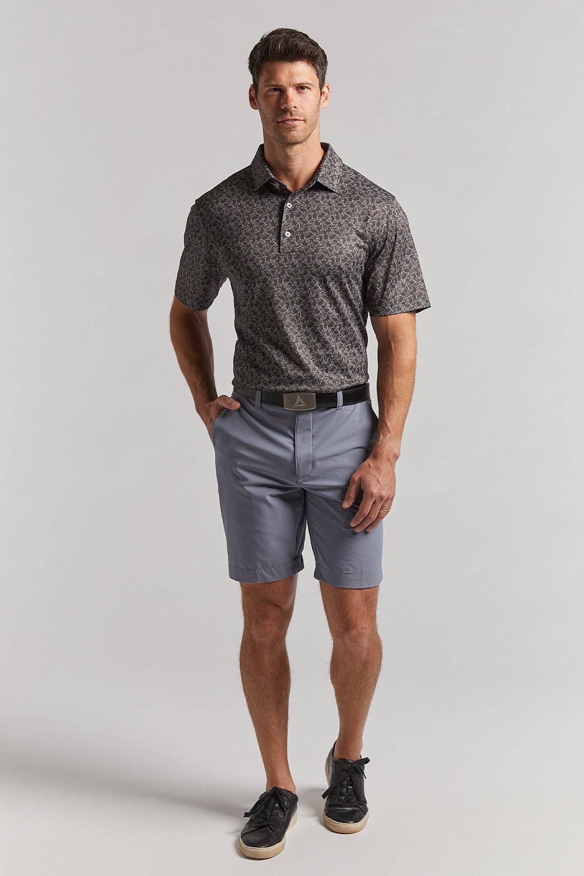 Man wearing a patterned polo shirt and light gray shorts on a plain background