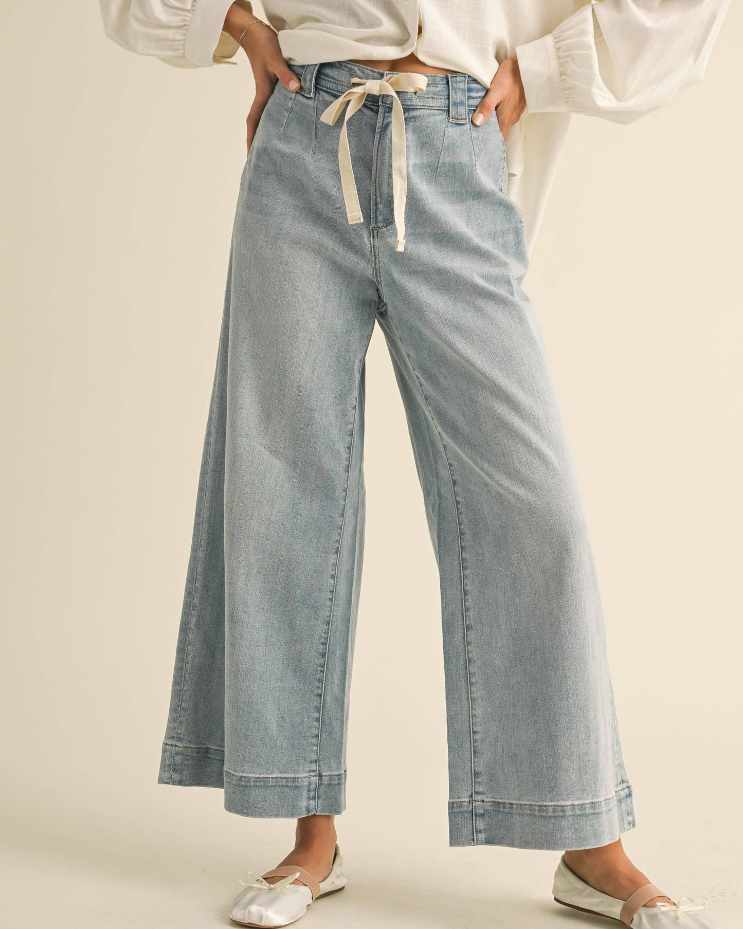 Person wearing light blue denim pants with a white shirt on a beige background