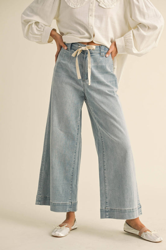 Person wearing light blue denim pants with a white shirt on a beige background