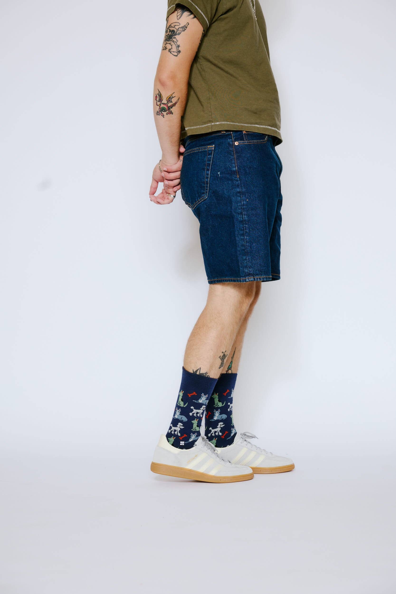 Person wearing a green t-shirt, blue denim shorts, and white sneakers with floral socks on a white background