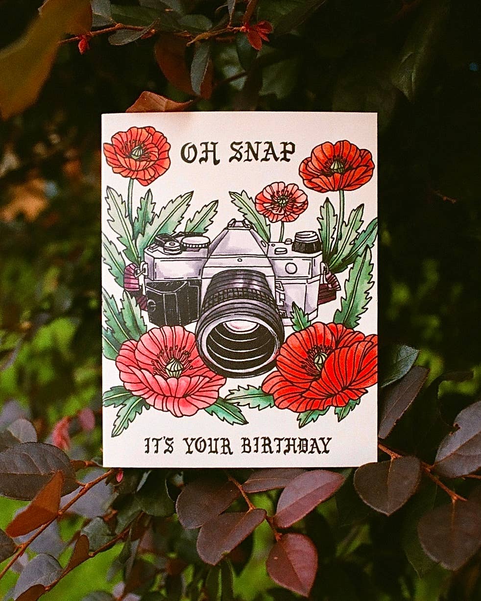 Greeting card with a camera and flowers on a leafy background