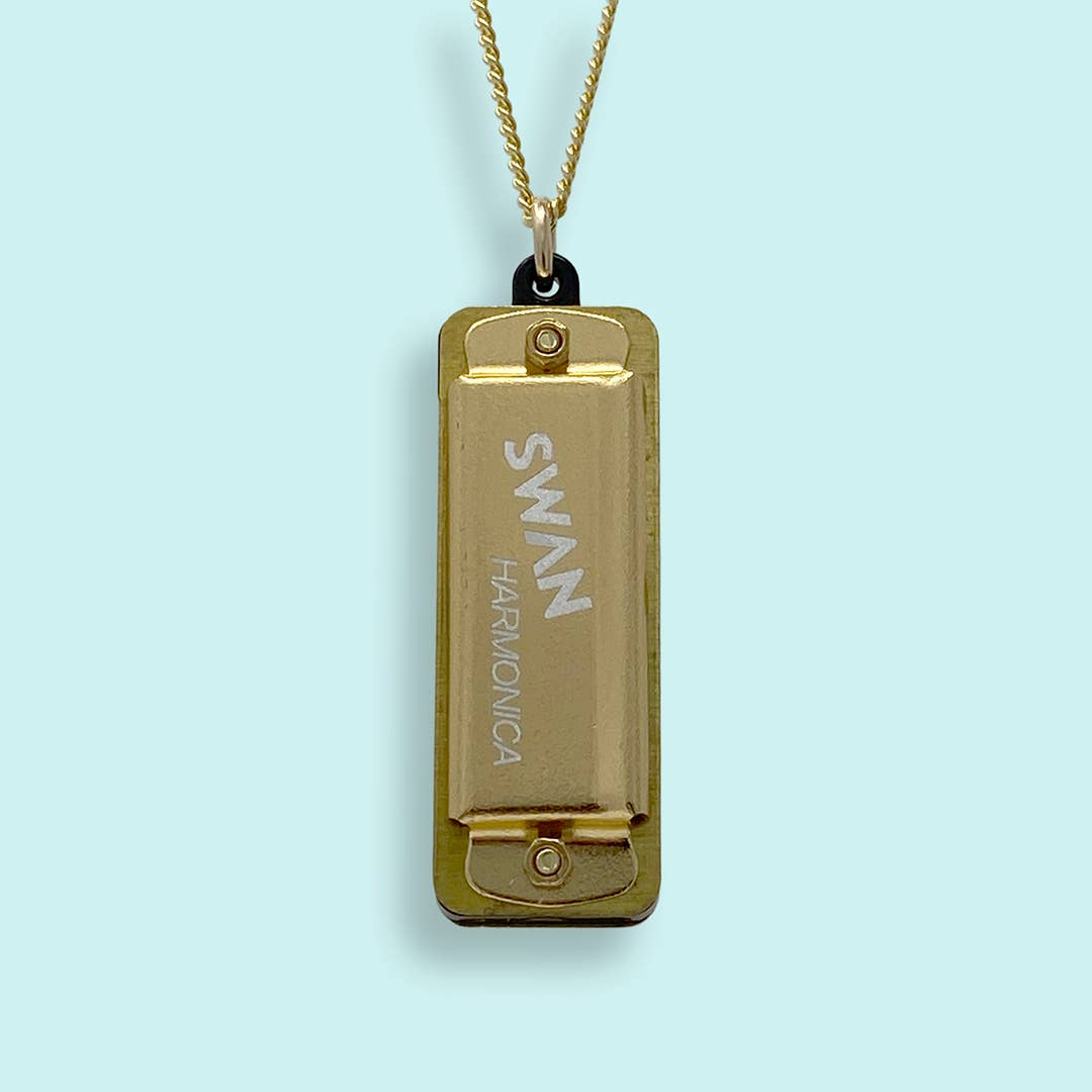 Gold Swan harmonica pendant on a light blue background