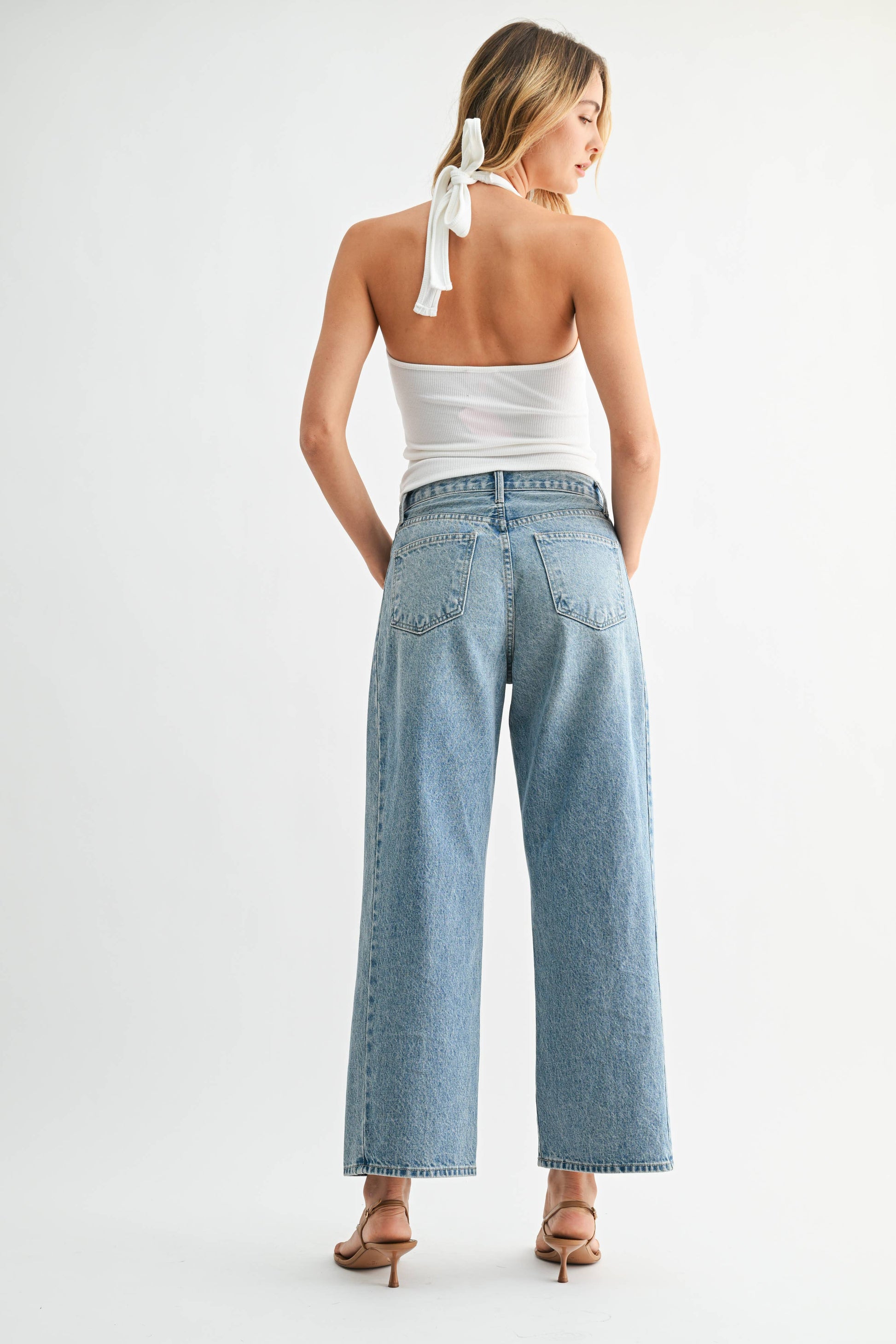 Woman wearing light blue jeans and a white top on a white background