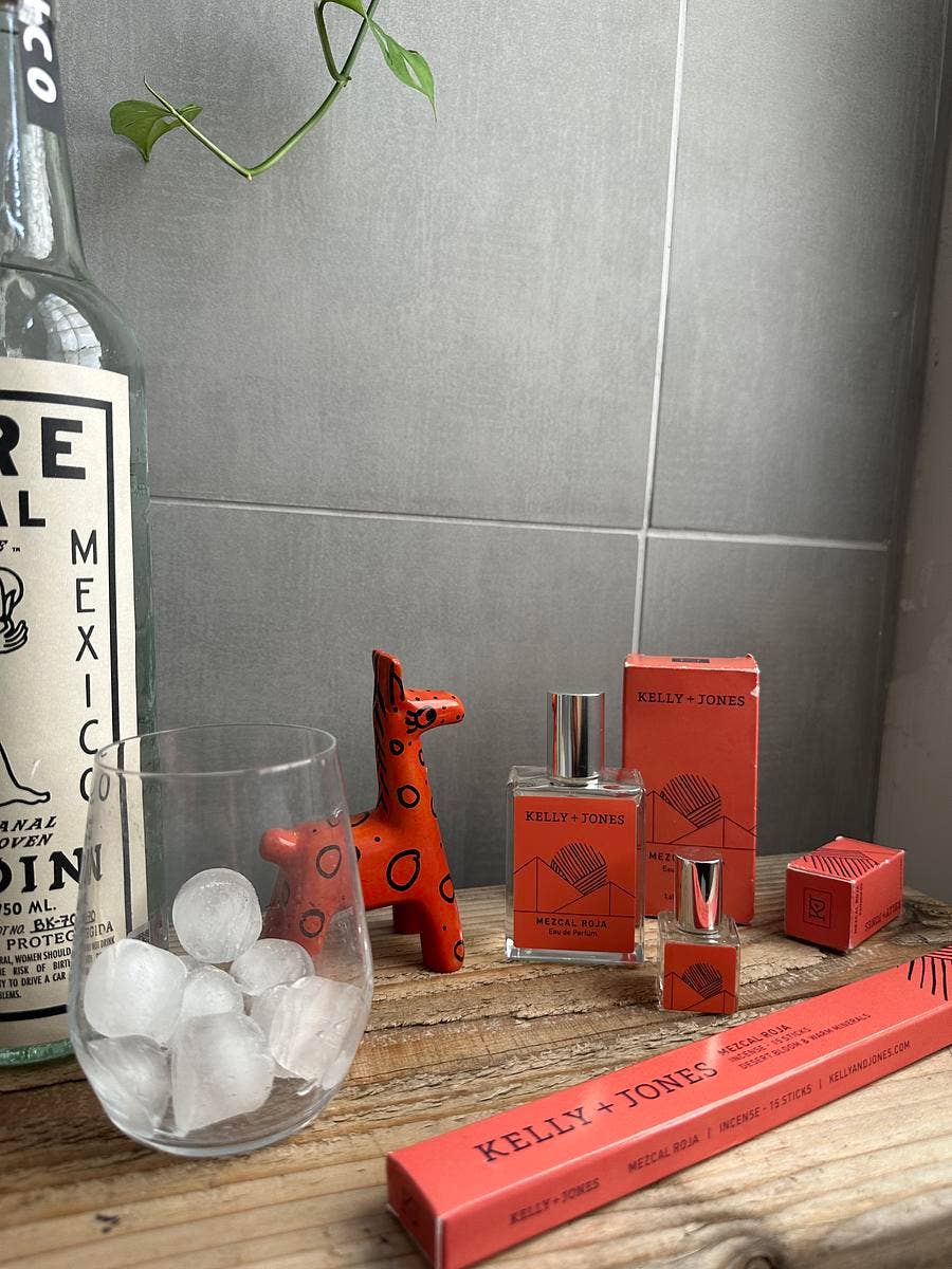 Kelly & Jones perfume bottles and packaging on a wooden surface with a bottle of tequila in the background.
