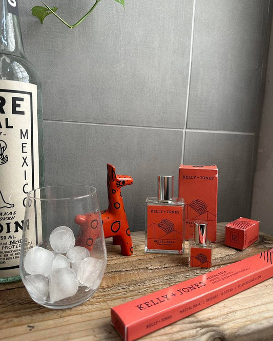 Kelly & Jones perfume bottles and packaging on a wooden surface with a bottle of tequila in the background.