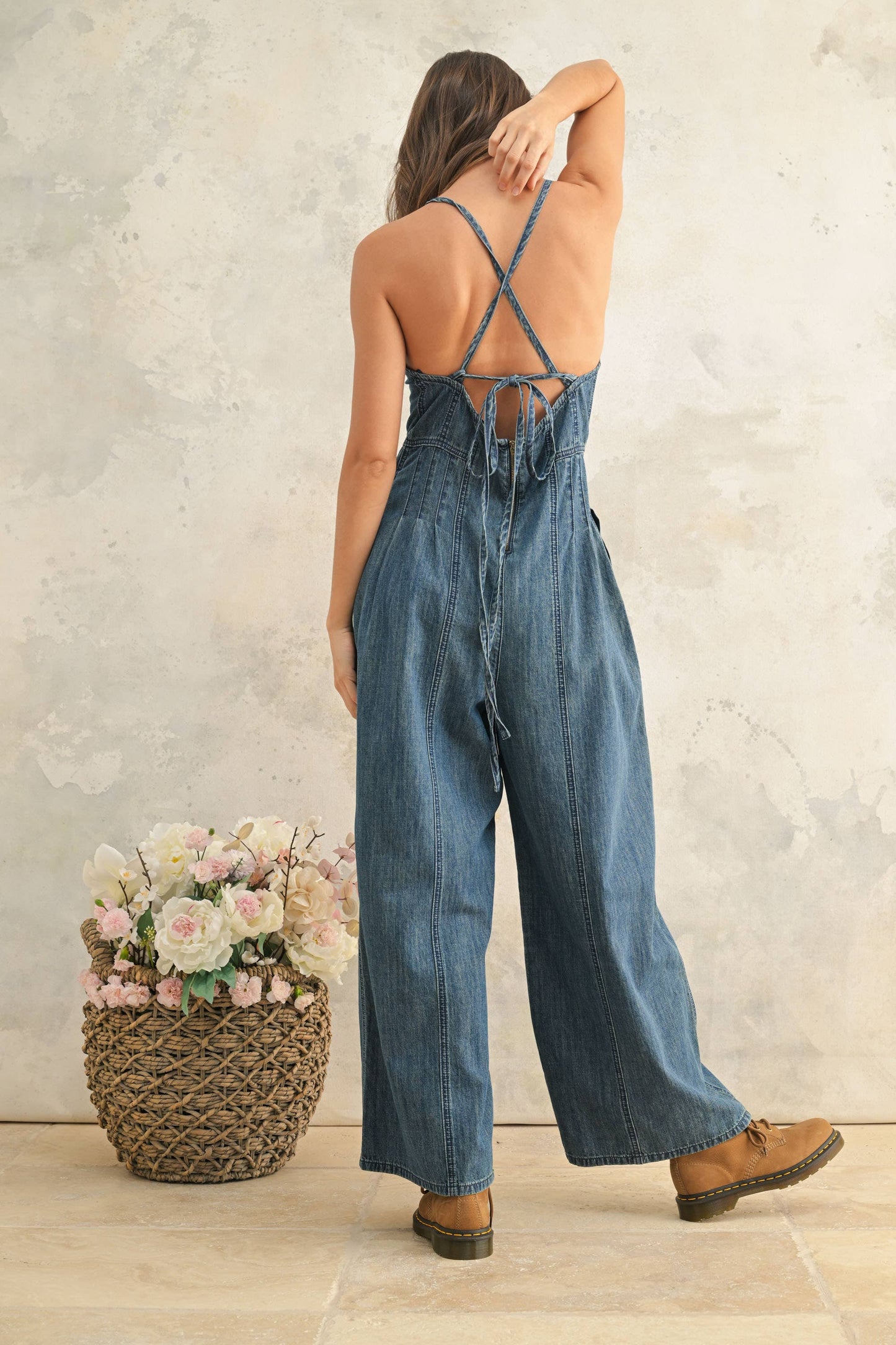 Woman wearing a denim jumpsuit with a floral arrangement in the foreground