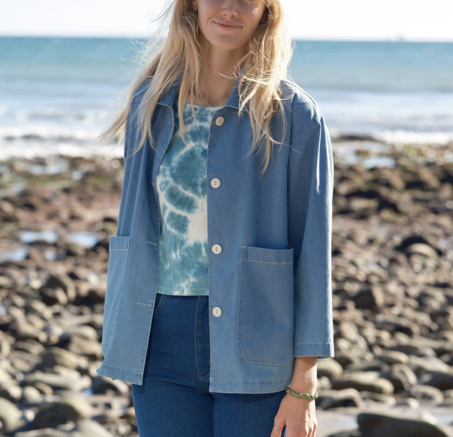 Women standing on the beach with a denim jacket, jeans and a blue and white tie-dye shirt.