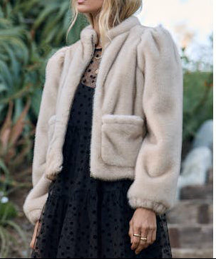 Woman wearing a beige fluffy jacket outdoors with greenery in the background