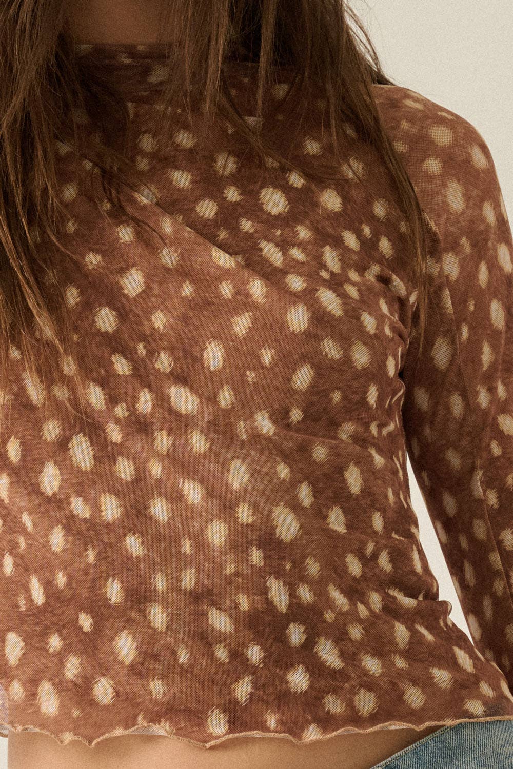 A close-up of a person wearing a brown long-sleeve mock-neck top with a beige tie-dye or watercolor dot pattern.