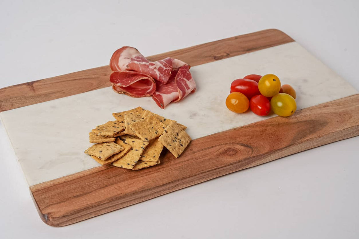 Wooden cutting board with prosciutto, crackers, and cherry tomatoes on a white background