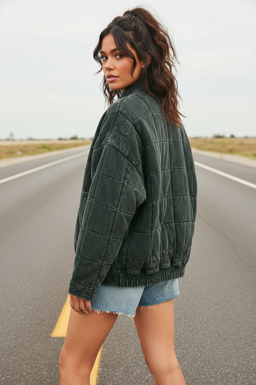 Person wearing a dark green quilted jacket and denim shorts on a beige background