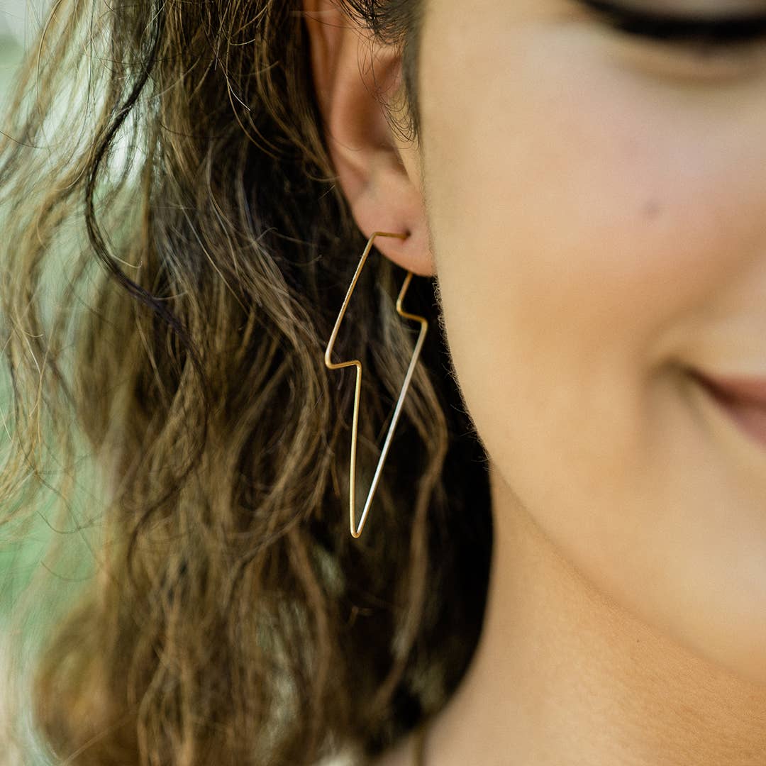 Close-up of a person wearing a gold geometric earring with a blurred background