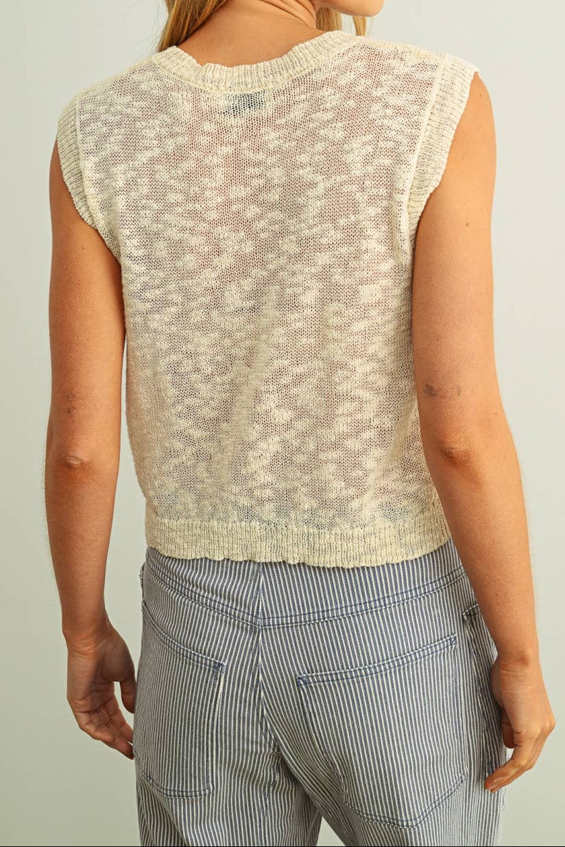 Woman wearing a beige sleeveless top with a subtle pattern against a plain background