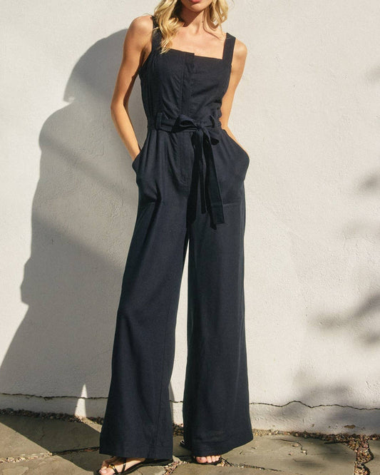 Woman wearing a black jumpsuit against a light wall.