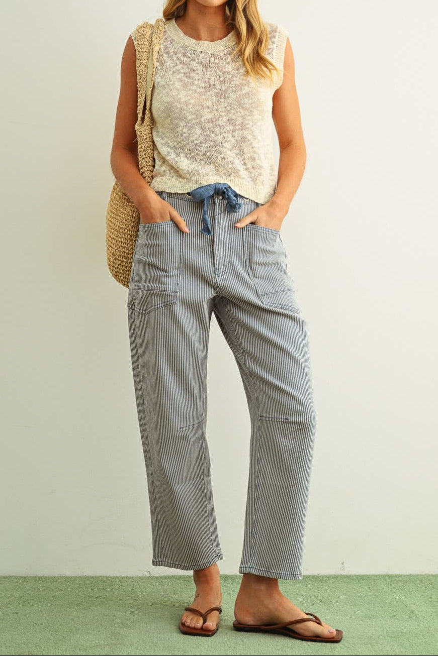 Woman wearing a sleeveless top and light blue jeans with a beige bag against a white background