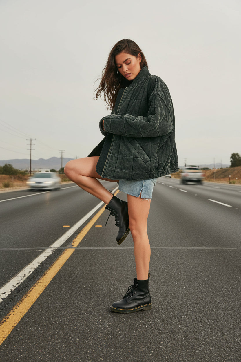 Woman wearing a dark green quilted jacket, denim shorts, and black boots on a beige background