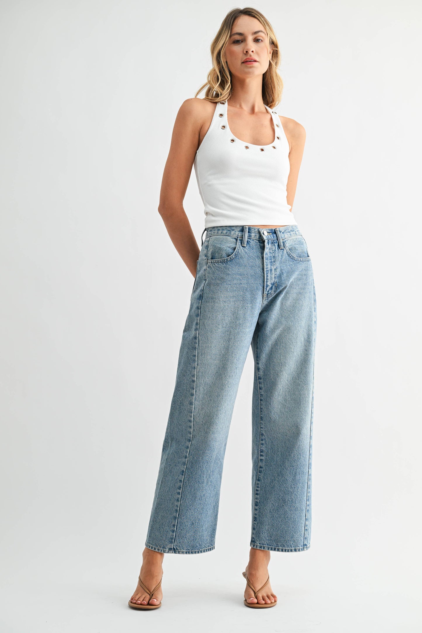 Woman wearing a white tank top and light blue jeans on a white background