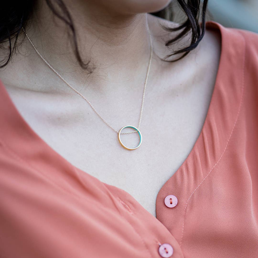 Necklace with a circular pendant worn by a person in a pink shirt.