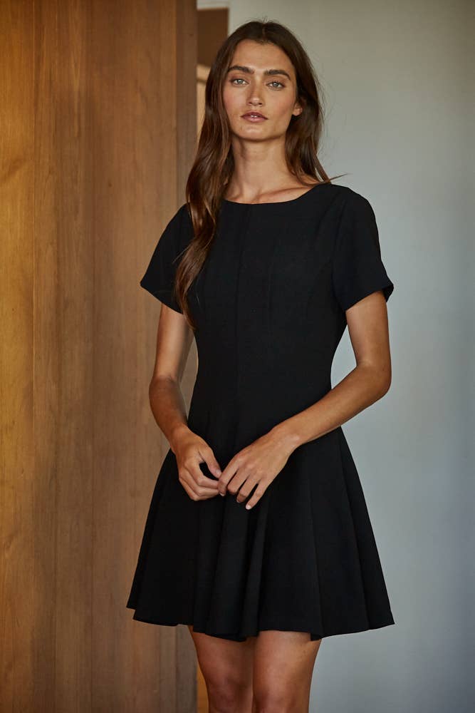 Woman wearing a black dress standing against a neutral background