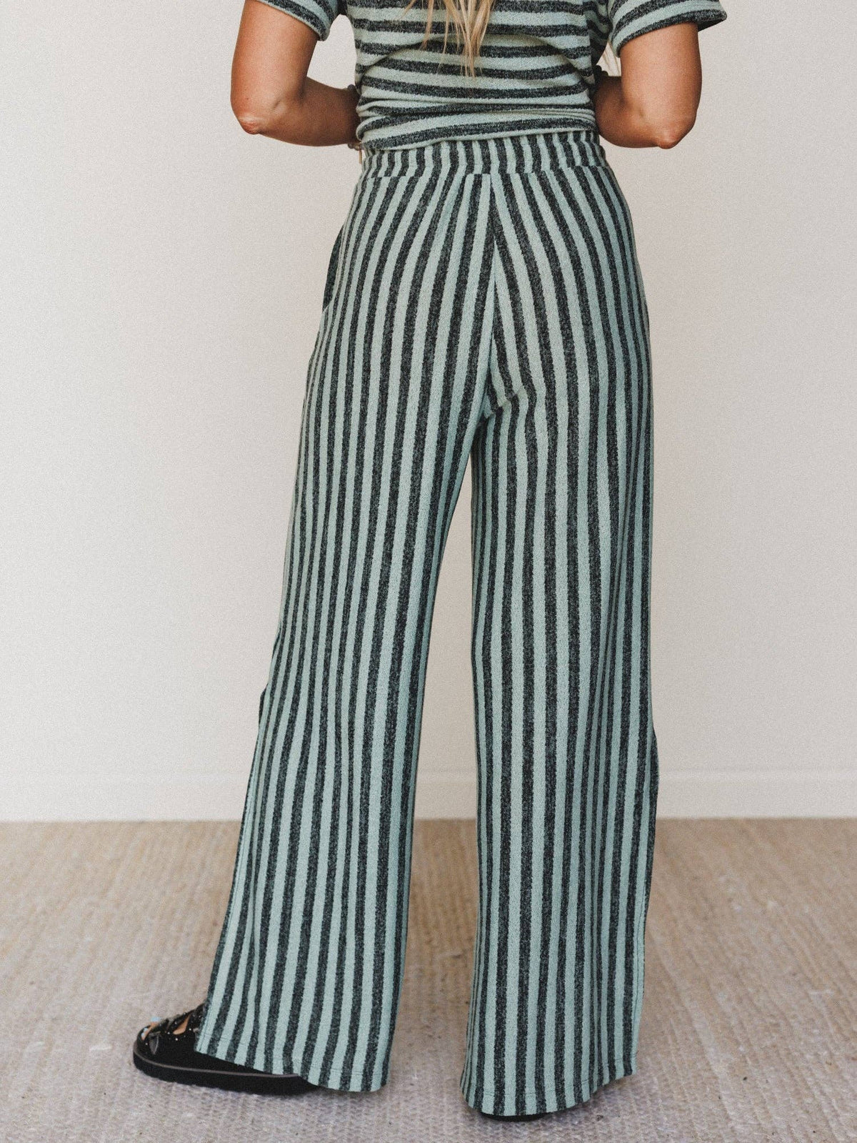 Person wearing a green and white striped outfit with wide-leg pants on a plain background
