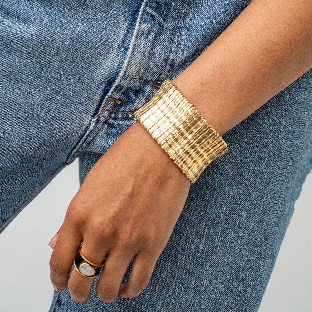 Gold bracelet and ring on a person's wrist with a denim background