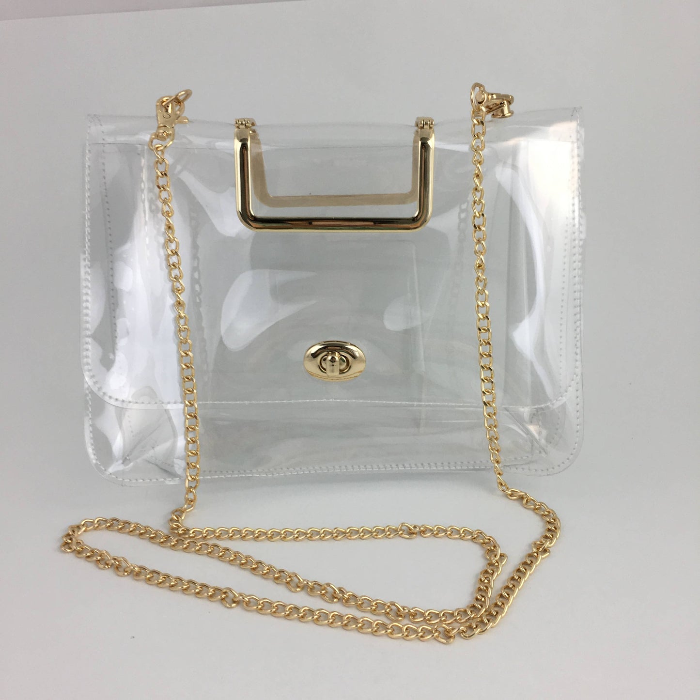 Clear vinyl handbag with a gold-tone metal handle, chain strap, and front clasp, photographed on a plain light background.