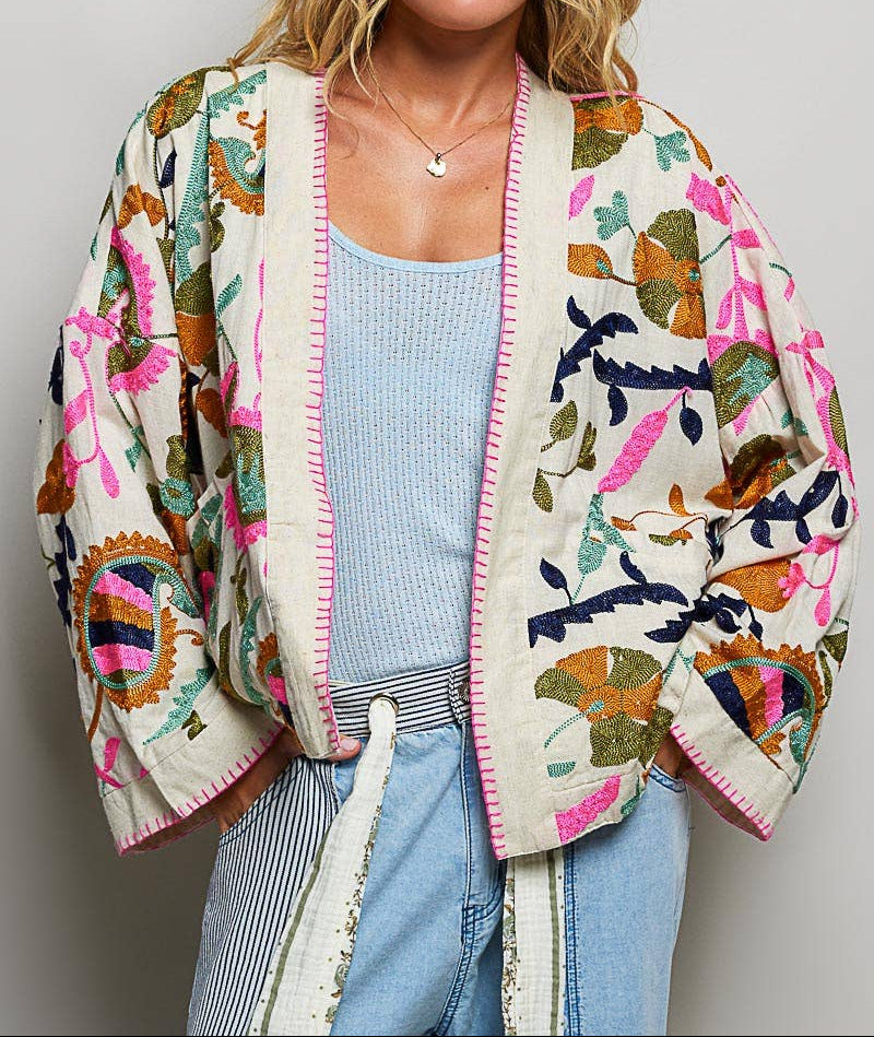 Woman wearing a colorful patterned cardigan over a light blue top and jeans on a plain background