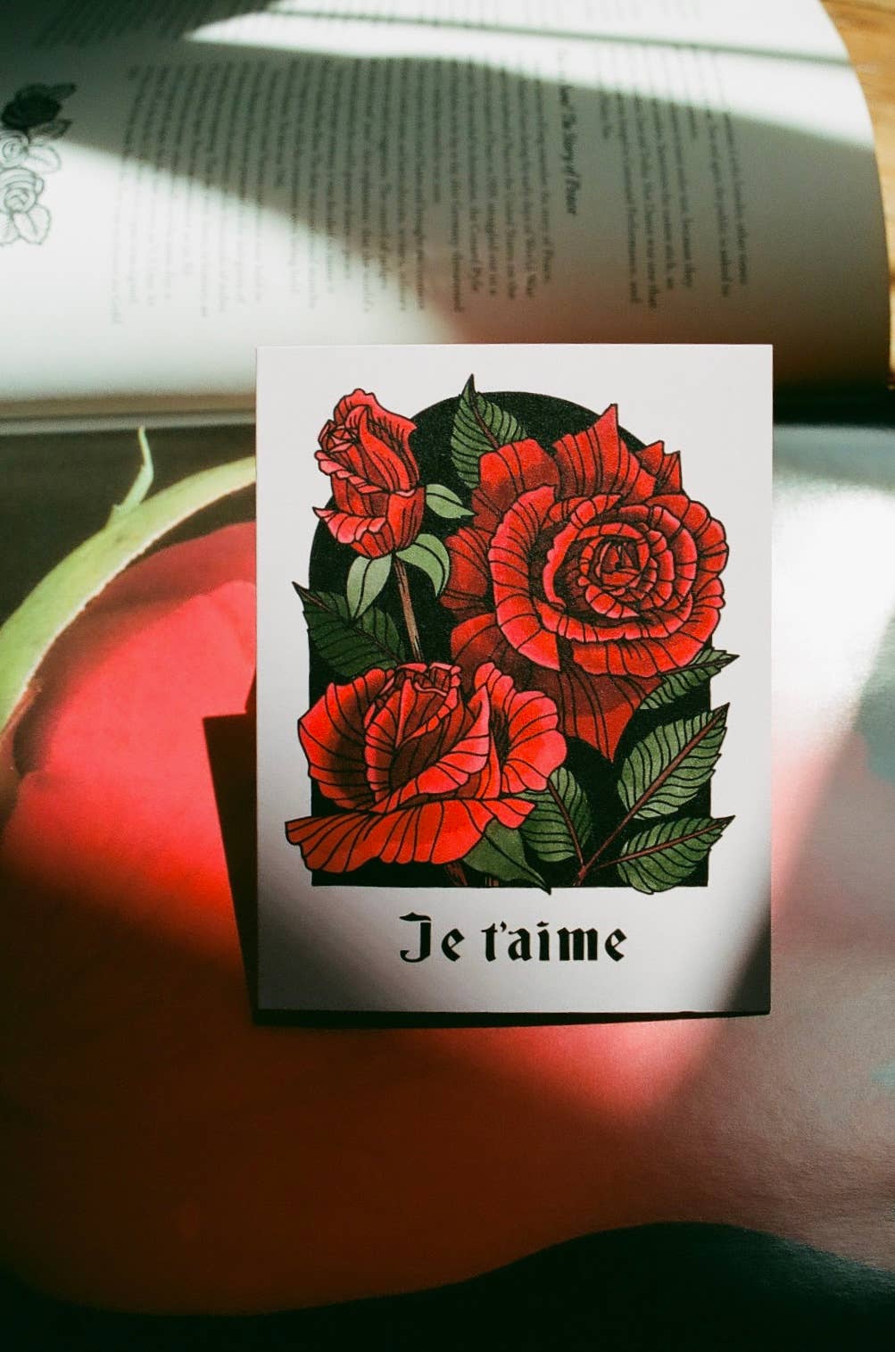 Card with red roses and 'Je t'aime' text on a book
