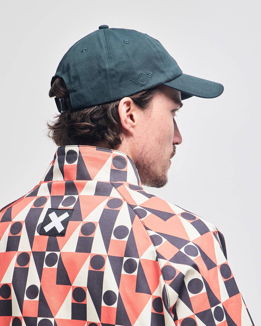 Person wearing a dark green cap and a patterned jacket with geometric design.