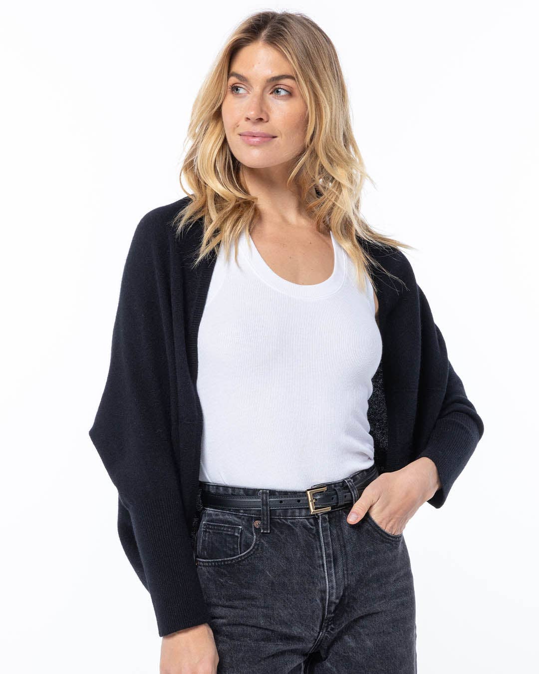 Woman wearing a black cardigan over a white shirt and dark jeans on a white background