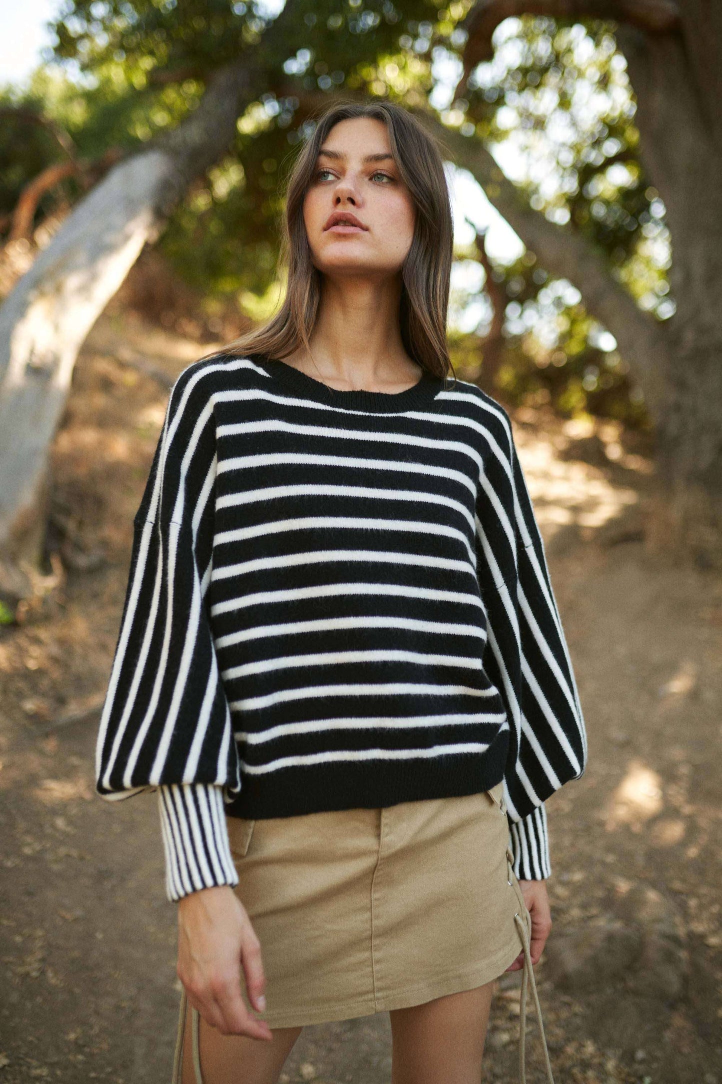 Woman wearing a black and white striped sweater and beige skirt outdoors.