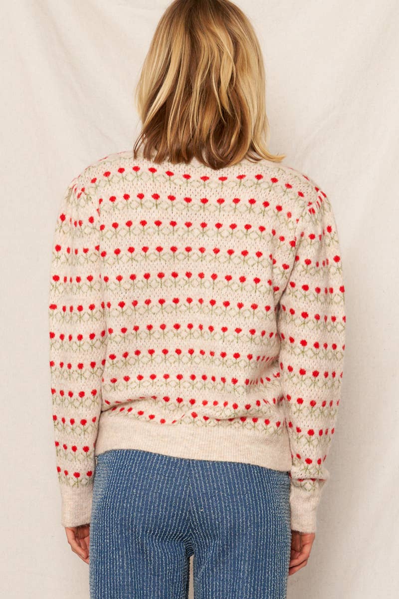 Person wearing a patterned sweater with red and beige design against a plain background