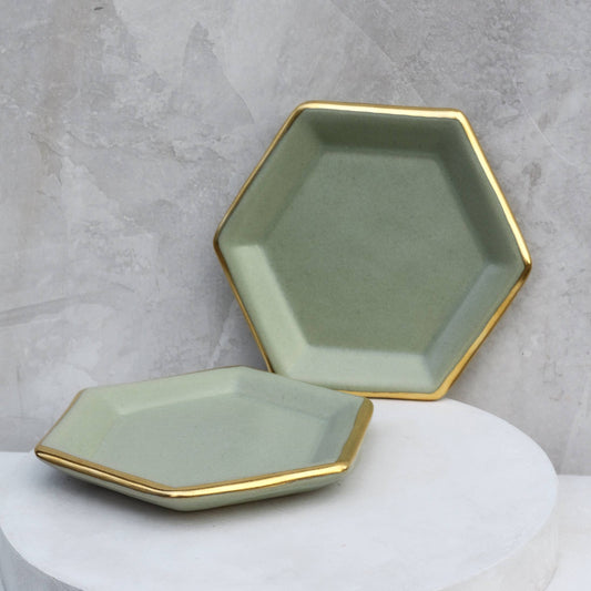 Two hexagonal ceramic trays with gold edges on a gray background