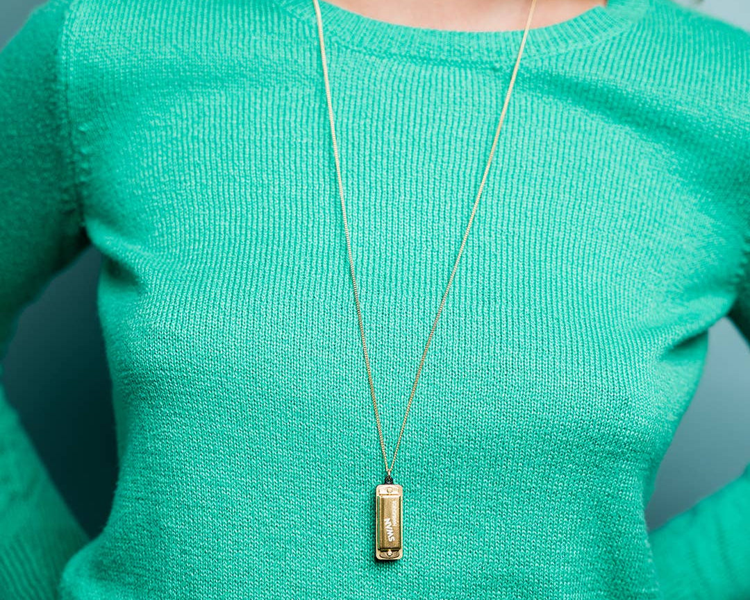Person wearing a green sweater with a gold necklace featuring a rectangular pendant.