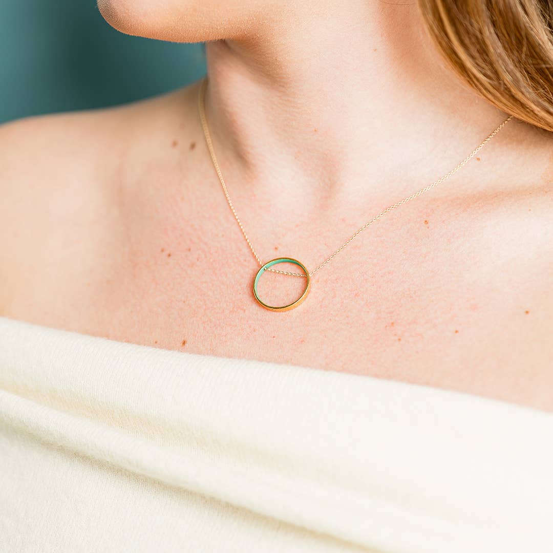 Gold necklace with a circular pendant on a person wearing a white top.
