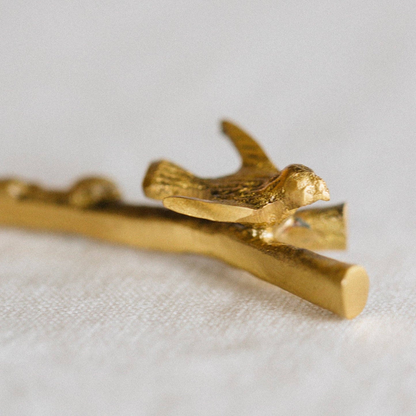 Gold bird figurine on a branch against a light background