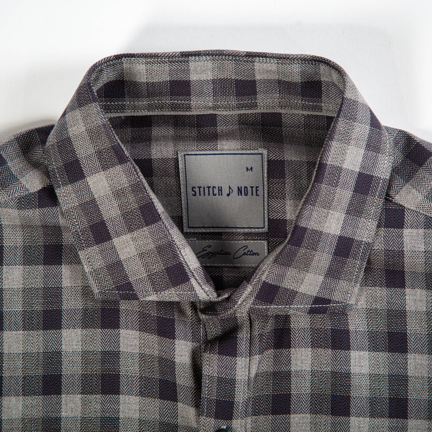 Gray and black plaid shirt with 'Stitch & Note' label on a white background