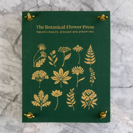 Green book titled 'The Botanical Flower Press' with gold floral illustrations on a marble background