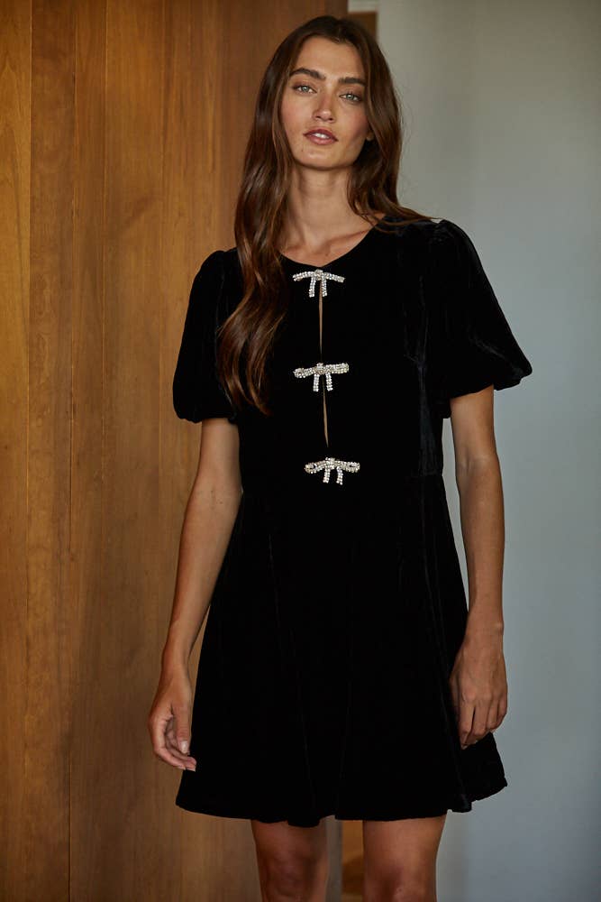 Woman wearing a black dress with white accents against a wooden wall.