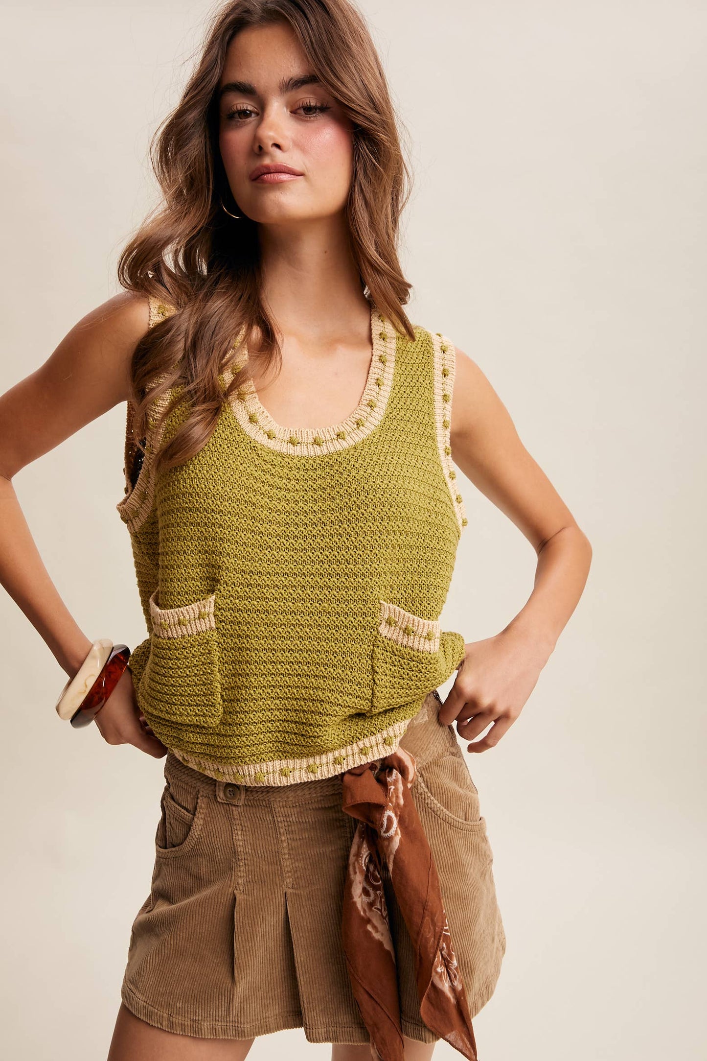 Woman wearing a green knitted tank top with beige accents on a plain background