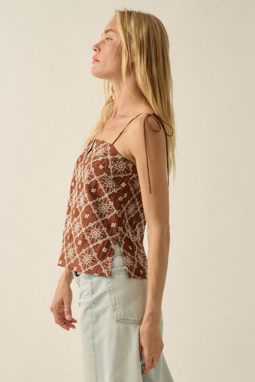 Woman wearing a patterned top and light jeans against a plain background