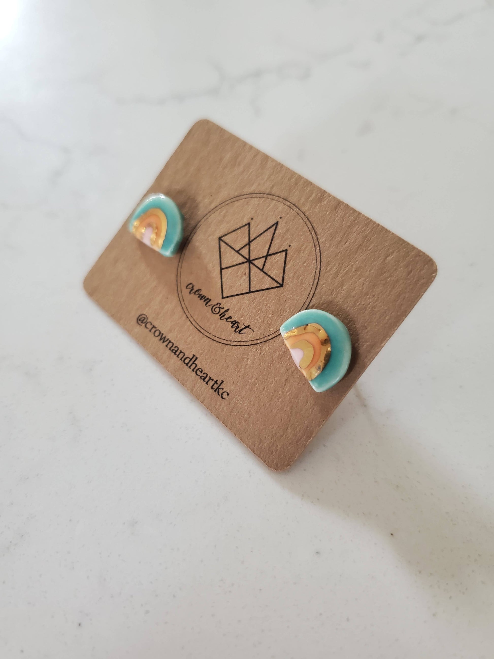 Pair of earrings on a branded card with a geometric design on a light background