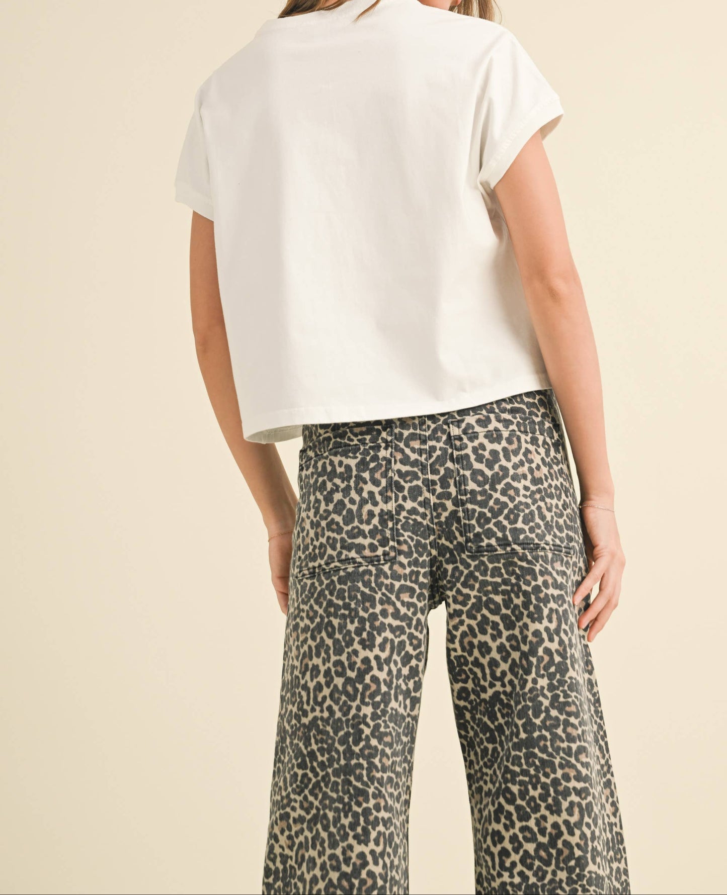 Woman wearing a white top and leopard print pants on a beige background