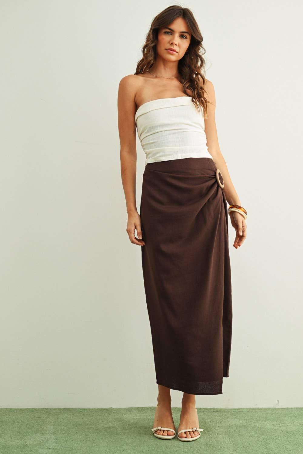 Woman wearing a white strapless top and brown skirt on a plain background