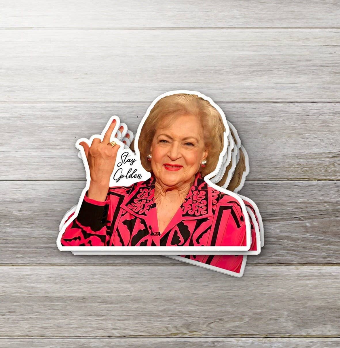 Sticker of a woman in a pink jacket with 'Stay Golden' text on a wooden surface