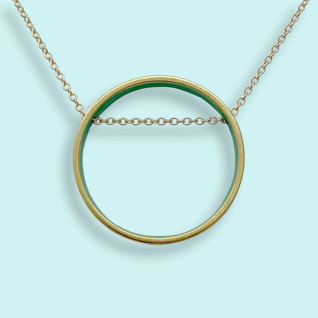 Gold necklace with a large circular pendant on a light blue background