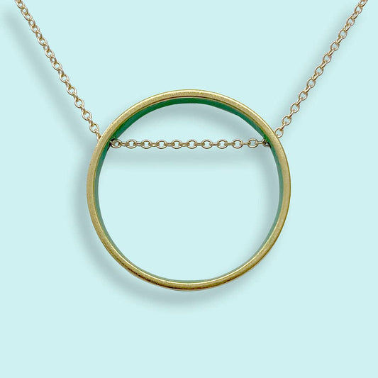 Gold necklace with a large circular pendant on a light blue background