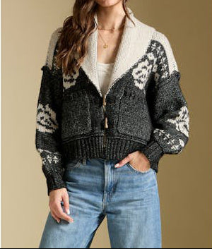 Woman wearing a patterned cardigan over a white shirt with blue jeans on a beige background