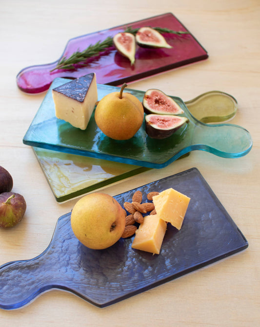 Glass cutting boards with fruit and cheese on a wooden surface